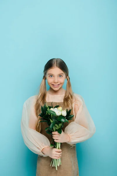 Happy kid holding bouquet of flowers on blue — Stock Photo