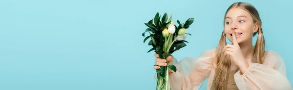 Colpo panoramico di bambino felice guardando mazzo di tulipani e mostrando segno di silenzio isolato su blu — Foto stock