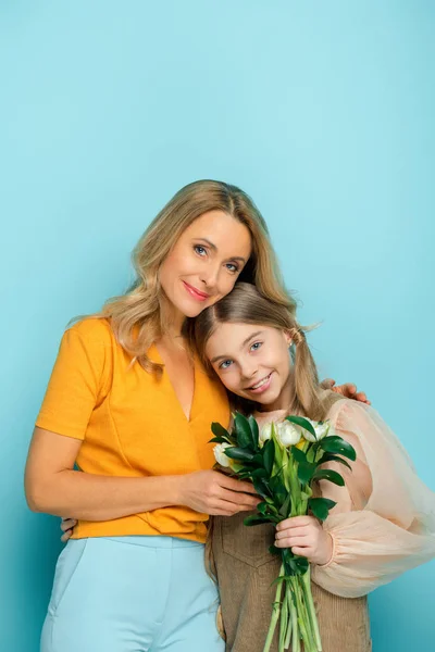 Allegra madre sorridente vicino figlia con tulipani isolati su blu — Foto stock