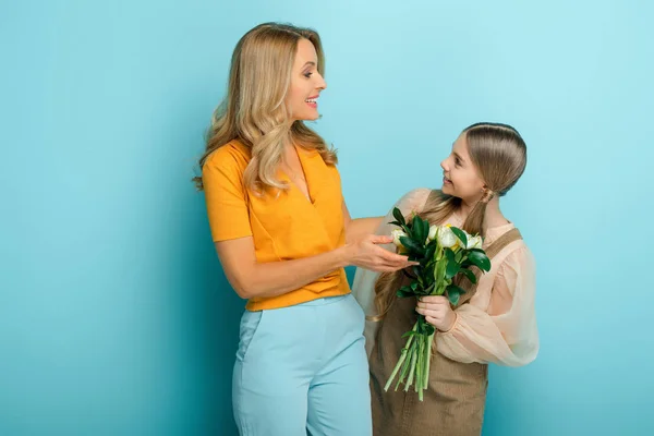 Щаслива мати дивиться на дочку з тюльпанами на синьому — стокове фото