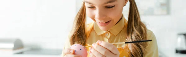 Tiro panorámico de niño feliz pintando huevo de Pascua con pincel - foto de stock