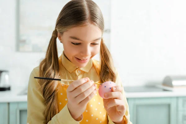 Щаслива дитина малює пасхальне яйце з пензлем вдома — стокове фото