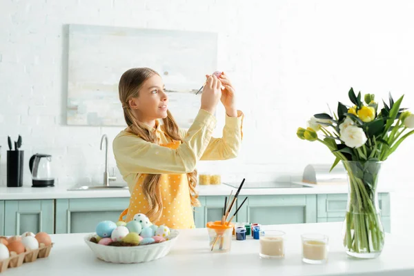 Adorable niño pintando huevo de Pascua con pincel cerca de tulipanes — Stock Photo