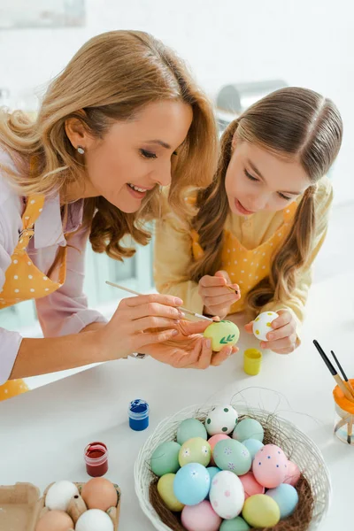 Happy mother and adorable daughter painting chicken eggs on easter — Stock Photo