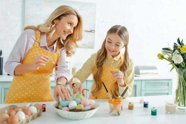 Mãe feliz olhando para a filha tomando ovos de páscoa pintados — Fotografia de Stock