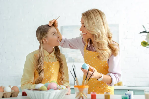 Selective focus of happy mother holding paintbrush near happy daughter and chicken eggs on easter — Stock Photo