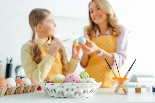 Fuoco selettivo di cesto con uova di Pasqua dipinte vicino a madre e figlia felice — Foto stock