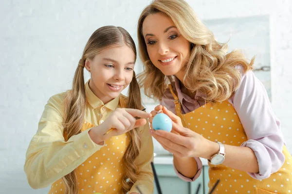 Niño feliz apuntando con el dedo al huevo de Pascua pintado cerca de la madre - foto de stock