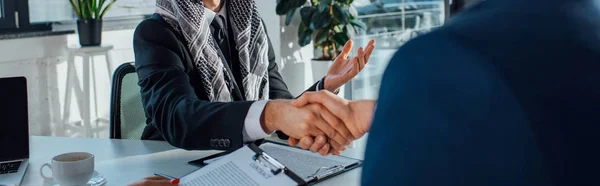 Panoramic shot of multiethnic businessmen shaking hands and having deal on meeting — Stock Photo