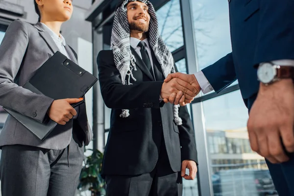Empresário árabe alegre apertando as mãos com parceiro em reunião com tradutor no escritório — Fotografia de Stock