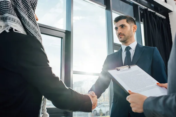 Hombre de negocios árabe estrechando la mano con el socio en la reunión con el traductor en la oficina - foto de stock