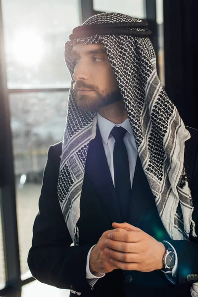 Guapo árabe hombre de negocios de pie en la oficina con luz de fondo - foto de stock