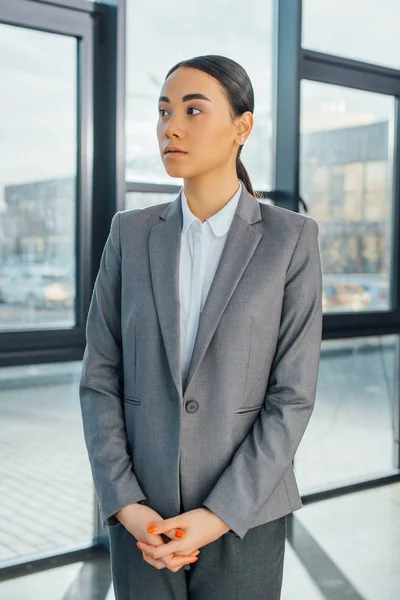 Азіатська бізнес-леді в сірому костюмі стоїть в сучасному офісі — стокове фото