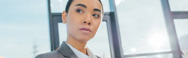 Панорамный снимок профессиональной азиатской предпринимательницы в сером костюме, стоящей в современном офисе — стоковое фото
