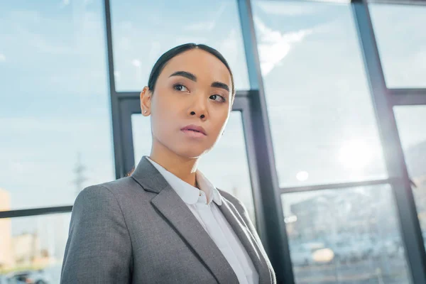 Executive asian businesswoman in grey suit standing in modern office — Stock Photo