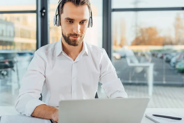 Traduttore maschio che lavora online con cuffie e laptop in ufficio — Foto stock