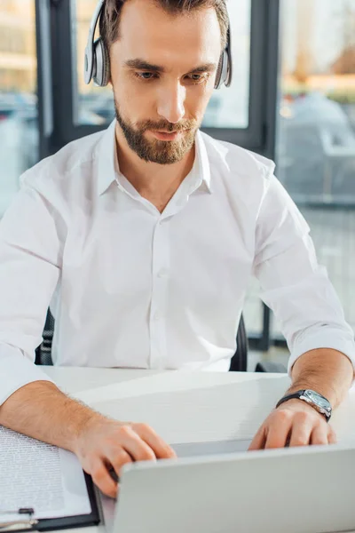 Traducteur professionnel travaillant en ligne avec écouteurs et ordinateur portable dans le bureau — Photo de stock