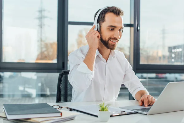 Professionelle fröhliche Übersetzer arbeiten online mit Kopfhörern und Laptop im Büro — Stockfoto