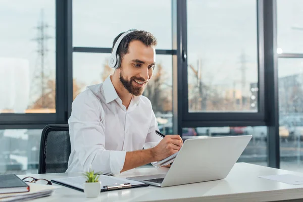 Positiver Übersetzer arbeitet online mit Kopfhörer und Laptop im Büro — Stockfoto
