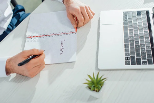 Partial view of translator writing in notepad in office with laptop and plant — Stock Photo