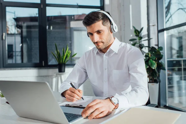 Guapo traductor masculino que trabaja en línea con auriculares y portátil - foto de stock