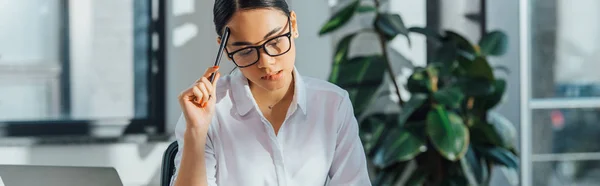 Plano panorámico de pensativo asiático traductor trabajando en oficina - foto de stock