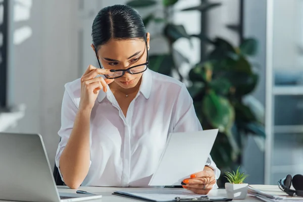 Traductor asiático en gafas de trabajo con ordenador portátil y documentos en la oficina - foto de stock