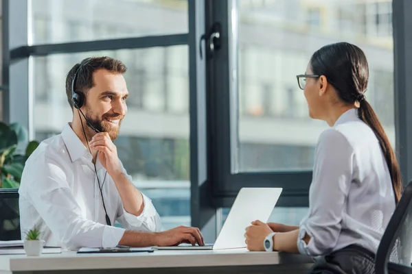 Traducteur masculin souriant travaillant en ligne avec ordinateur portable et casque lors d'une réunion avec une femme d'affaires — Photo de stock