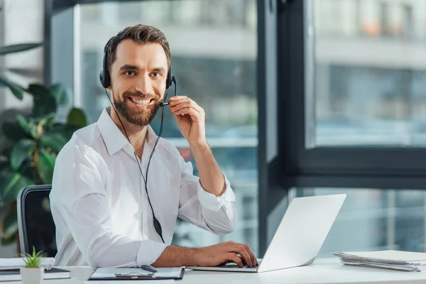 Fröhlicher männlicher Übersetzer in Brille, der online mit Headset und Laptop arbeitet — Stockfoto