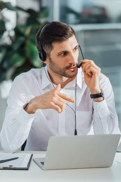 Guapo traductor masculino que trabaja en línea con auriculares y portátil - foto de stock