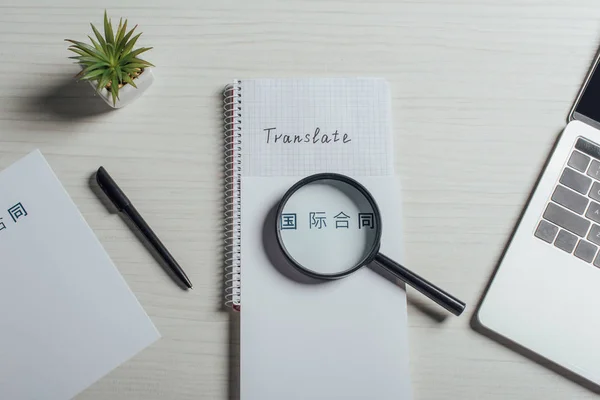 Top view of hieroglyphics, magnifier and laptop on translator workplace — Stock Photo