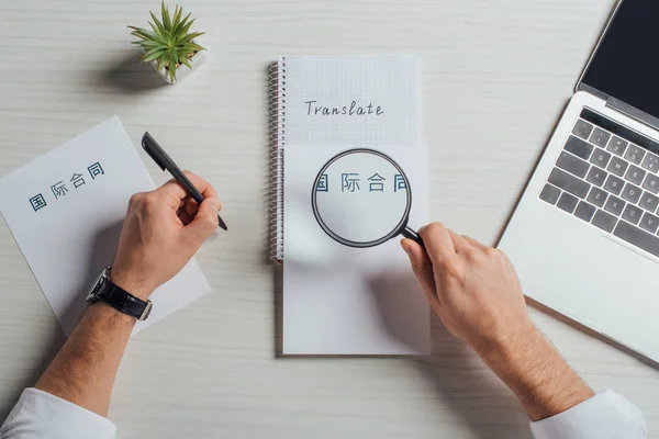 Cropped view of translator working with hieroglyphics, laptop and magnifying glass — Stock Photo