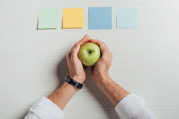 Partial view of businessman holding apple on table with note stickers — Stock Photo