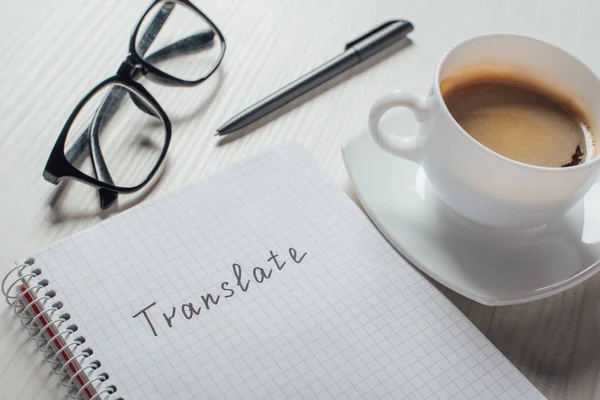 Close up of coffee and notepad with word translate on workplace — Stock Photo