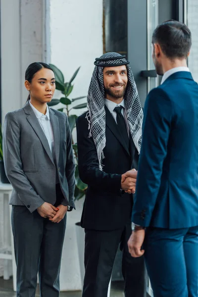Мультиэтнические улыбающиеся деловые партнеры пожимают руку на встрече с переводчиком в офисе — стоковое фото