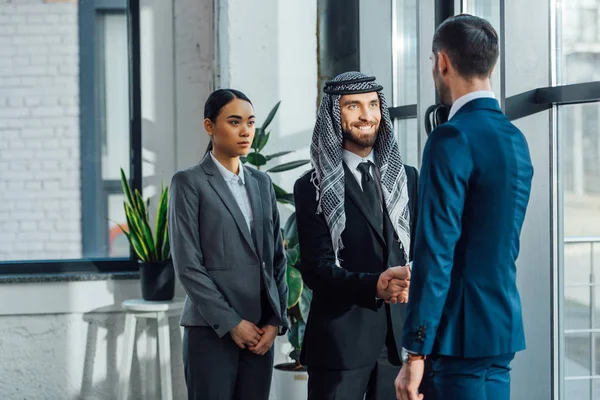 Smiling multicultural business partners shaking hands and having deal with translator in office — Stock Photo