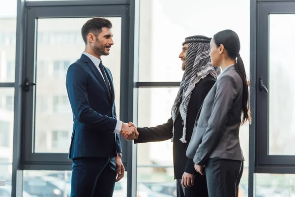 Socios comerciales multiculturales profesionales estrechando la mano en la reunión con el traductor en la oficina - foto de stock