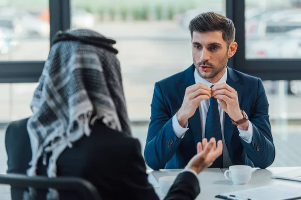 Hombre de negocios de Oriente Medio hablando con el socio en la reunión en la oficina moderna - foto de stock