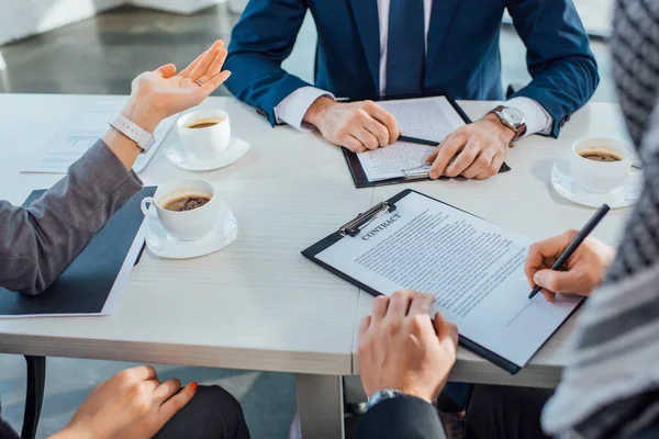 Cropped view of professional business partners signing contract on meeting in office with coffee cups — Stock Photo