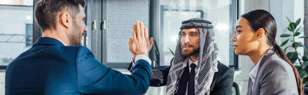 Panoramic shot of professional multicultural business partners giving highfive on meeting with translator in office — Stock Photo