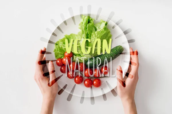 Top view of woman holding plate with raw vegetables on white background — Stock Photo