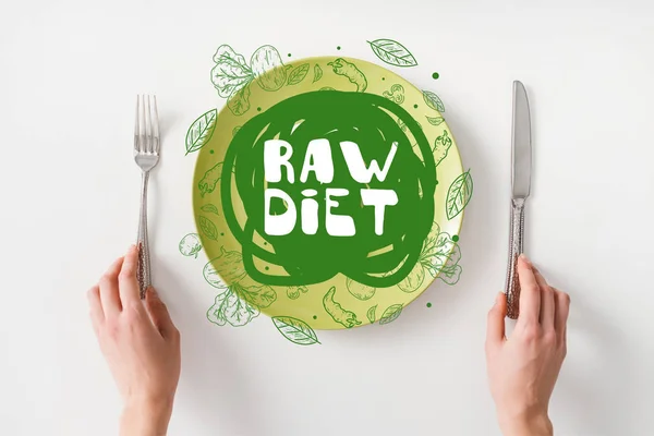 Top view of woman holding cutlery near smartphone on green plate on white background — Stock Photo