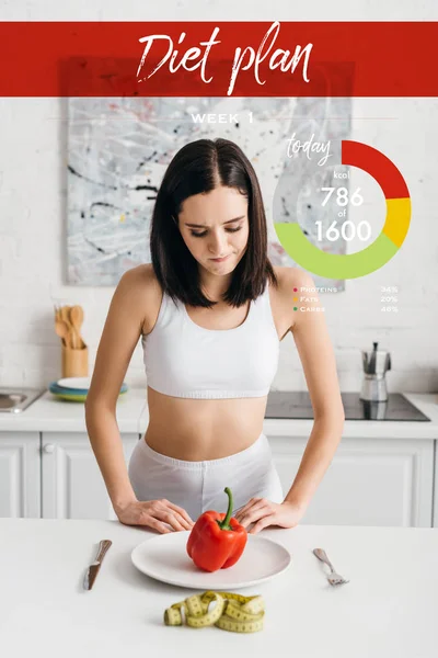 Selective focus of thoughtful sportswoman looking at bell pepper near measuring tape on kitchen table, diet plan illustration — Stock Photo