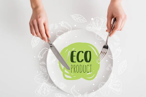 Vista dall'alto della donna che tiene posate su piatto con illustrazione di prodotto ecologico su sfondo bianco — Foto stock