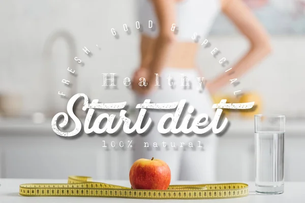 Foco selectivo de manzana, cinta métrica y vaso de agua cerca de deportista en forma en la cocina, iniciar ilustración dieta - foto de stock