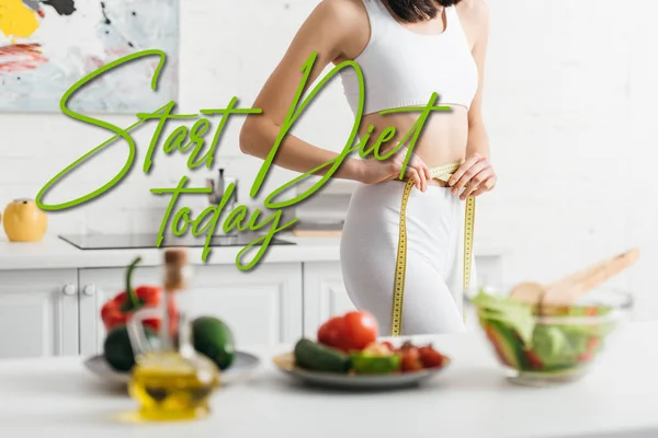 Concentration sélective d'une femme mince mesurant la taille avec du ruban adhésif près des légumes frais et de la salade sur la table, commencer l'alimentation aujourd'hui illustration — Photo de stock