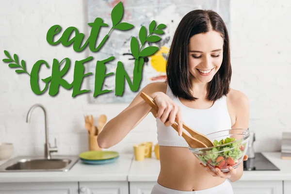 Attraktive fitte Sportlerin lächelt beim Mischen von Salat in der Küche, isst grüne Abbildung — Stockfoto