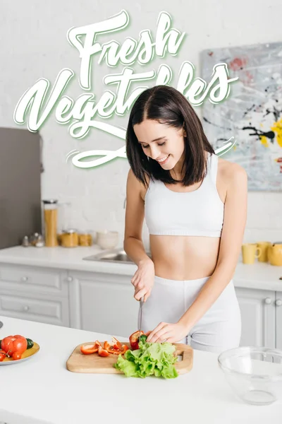 Jolie sportswoman mince souriant et cuisine salade avec illustration de légumes frais — Photo de stock