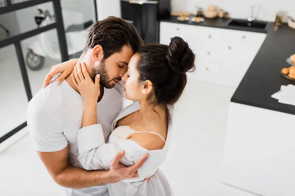Красивая женщина в лифчике и рубашке целуется с парнем на кухне — стоковое фото