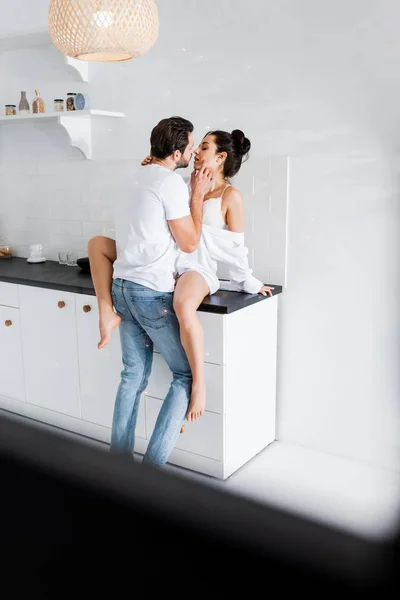 Selective focus of sexy woman in bra and shirt kissing boyfriend on kitchen worktop — Stock Photo